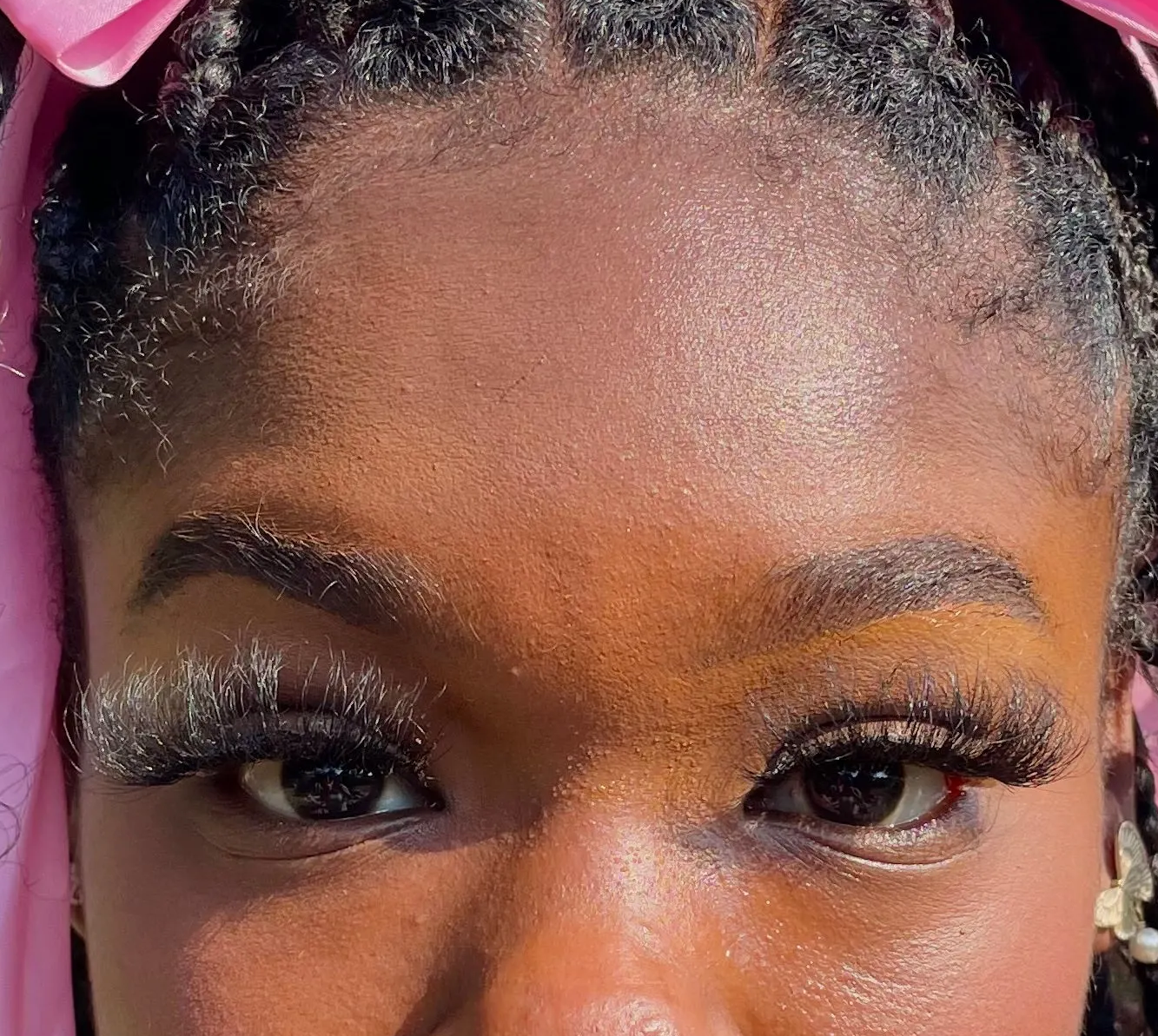Close-up of a person with braided hair and pink headband and false eyelashes 